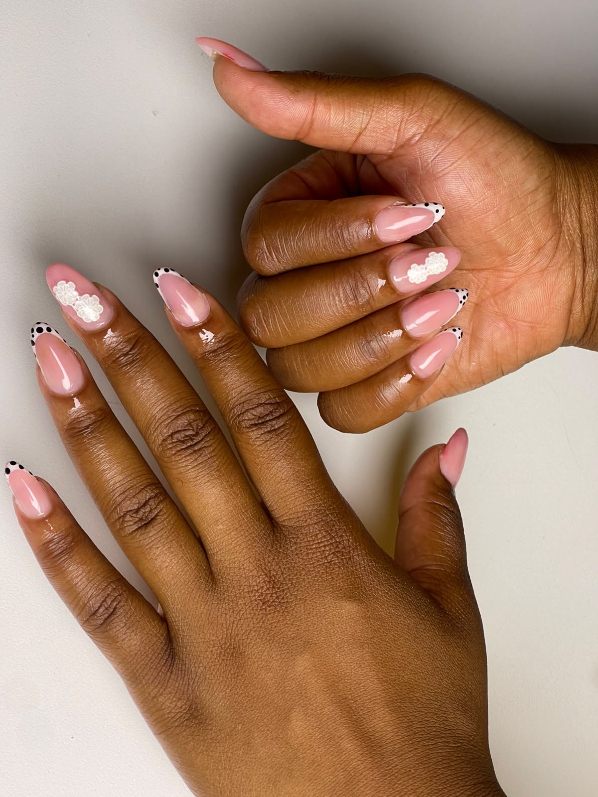 Short almond nails in sheer pink gel with black polka-dot French tips and white 3D flowers