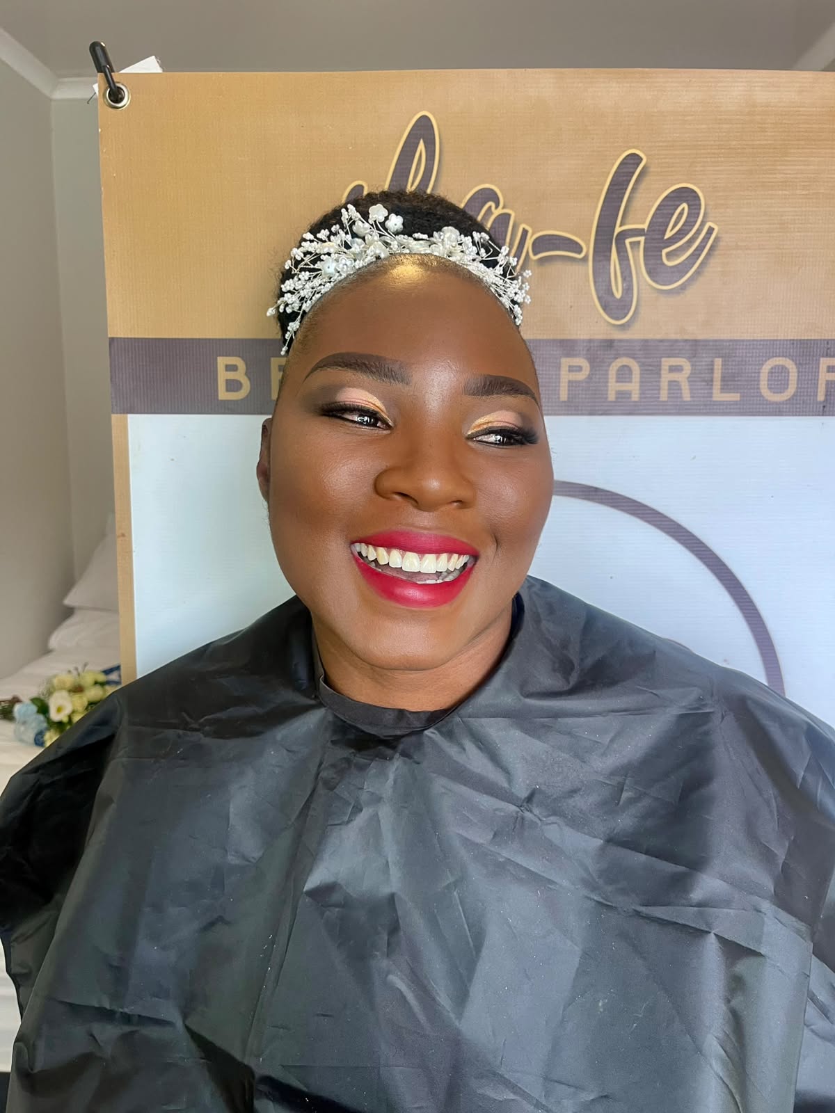 Smiling bride with gold eyes, a red lip and a pearl hair crown, in front of the La-fe banner